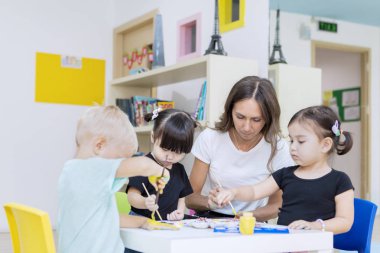 Anaokulu öğrencileri öğretmenleriyle resim yapıyor.