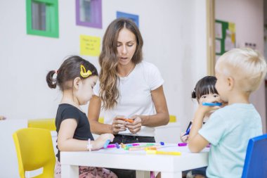 Anaokulu öğrencileri öğretmenleriyle birlikte boya kalemleri kullanıyor.