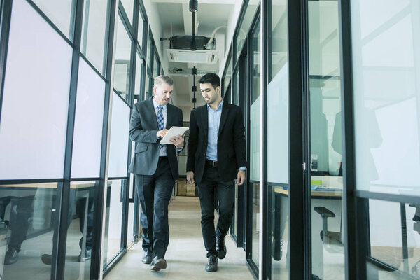 бизнесмены обсуждают работу во время прогулки по офисному коридору
