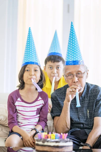 Büyükbaba ve torunlar korna çalıyor ve parti şapkası takıyorlar — Stok fotoğraf