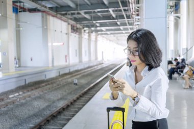 Tren istasyonunda cep telefonu kullanan Asyalı iş kadını
