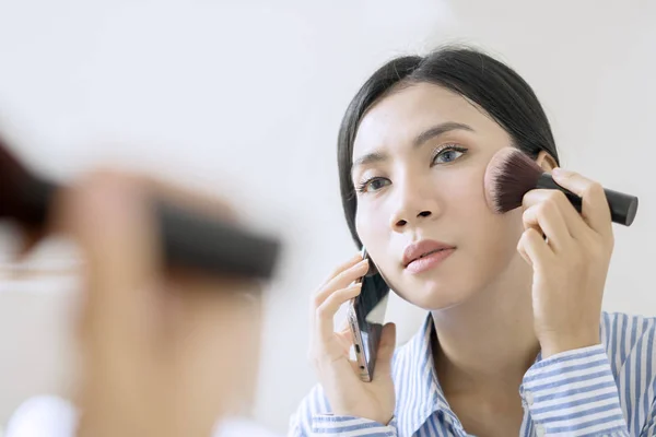 Attractive Asian businesswoman holding a blush brush while talking on the phone — Stock Photo, Image