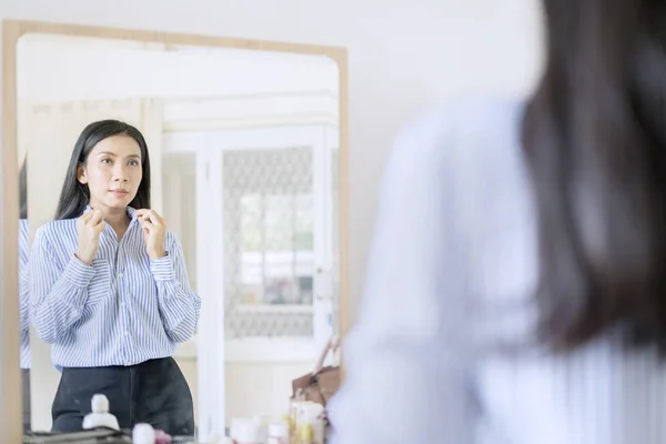 Элегантная азиатская деловая женщина, застегивающая рубашку перед зеркалом, готовится к работе — стоковое фото