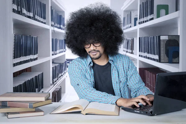 Άνδρας φοιτητής που σπουδάζει σε φορητό υπολογιστή στη βιβλιοθήκη — Φωτογραφία Αρχείου