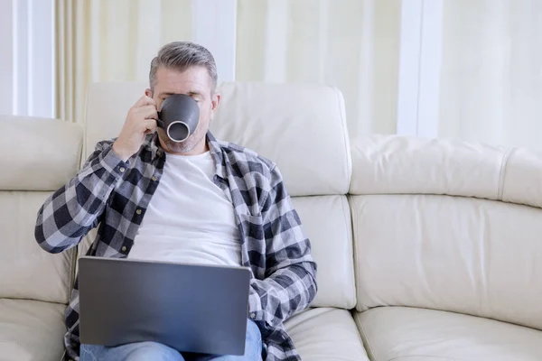 Muž pije čaj při práci na notebooku — Stock fotografie