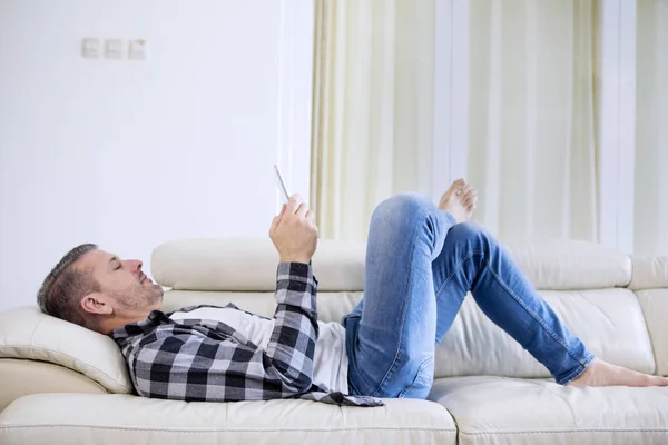 Человек лежит на диване смотреть на цифровой планшет — стоковое фото