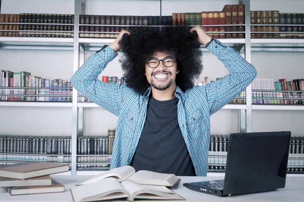 Student tahá za vlasy při studiu s knihami a notebookem v knihovně — Stock fotografie
