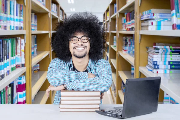 Φοιτητής με μεγάλα αφρο μαλλιά χέρια σταυρωμένα πάνω από τα βιβλία στη βιβλιοθήκη — Φωτογραφία Αρχείου