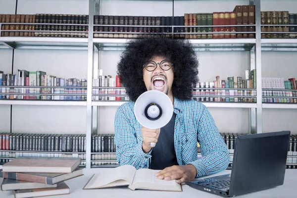 Studente maschio con grandi capelli afro urlando sul megafono mentre studiava in biblioteca — Foto Stock