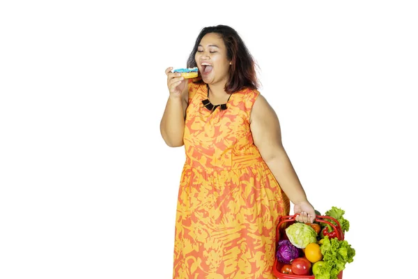 Mulher gorda mordendo donut enquanto carrega vitaminas — Fotografia de Stock