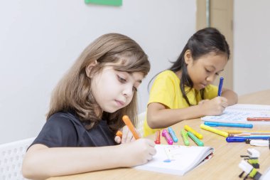 Kalemin rengini değiştirdikten sonra çizen iki çocuk