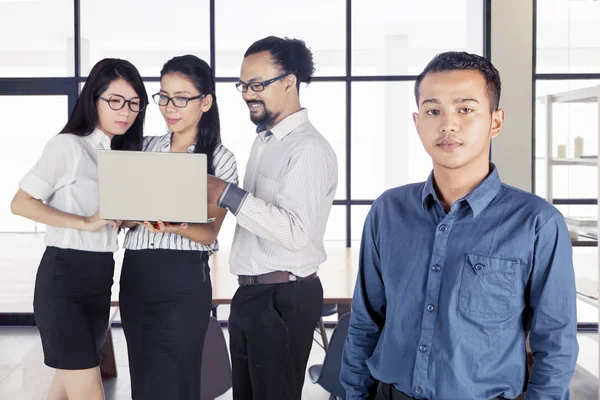 Drei Menschen arbeiten, während ein Mann in die Kamera starrt — Stockfoto