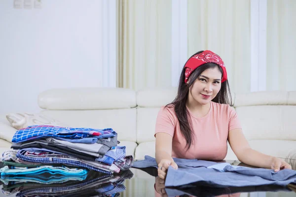 Mulher bonita sorrindo enquanto dobra roupas — Fotografia de Stock