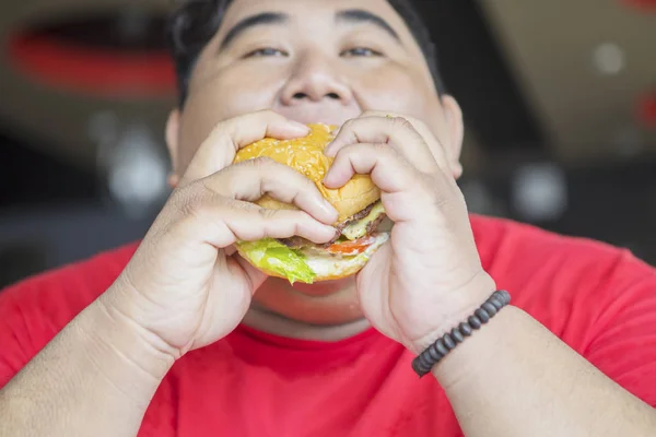 Närbild av fett asiatisk man äter en ostburgare — Stockfoto