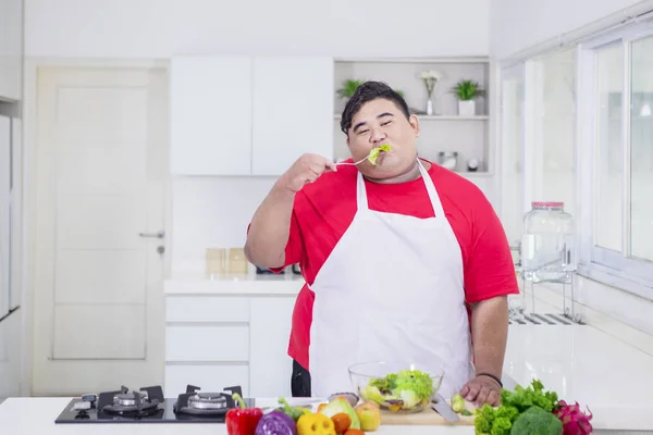 Fat Asian man biting a lettuce in the kitchen — Stock Photo, Image