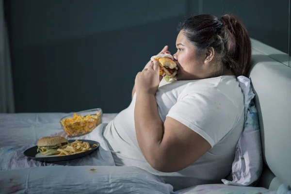 亚洲胖女人一边吃汉堡包一边看电视 — 图库照片