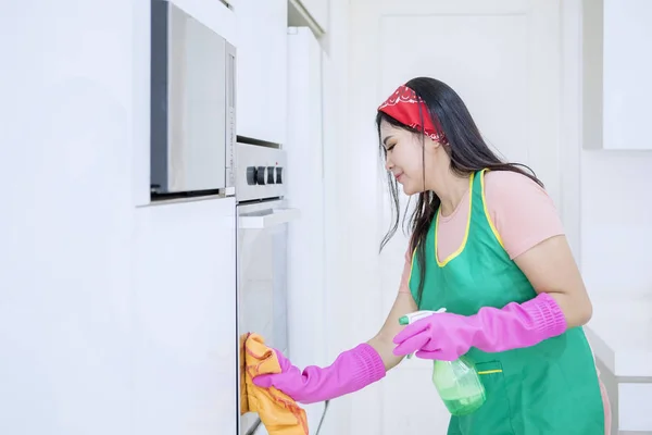 Oldalnézet ázsiai nő takarítás egy sütő — Stock Fotó