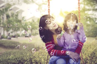 Anne köpük üflerken kızını tutuyor.