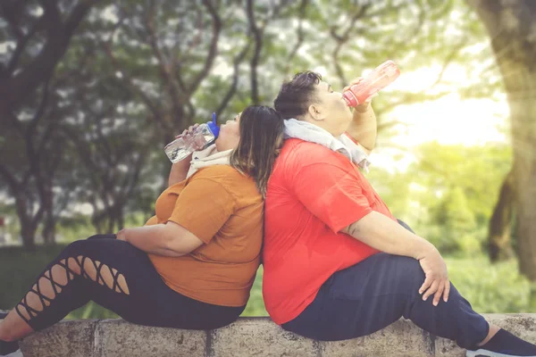 Gordura casal chugging água em um parque no dia ensolarado — Fotografia de Stock