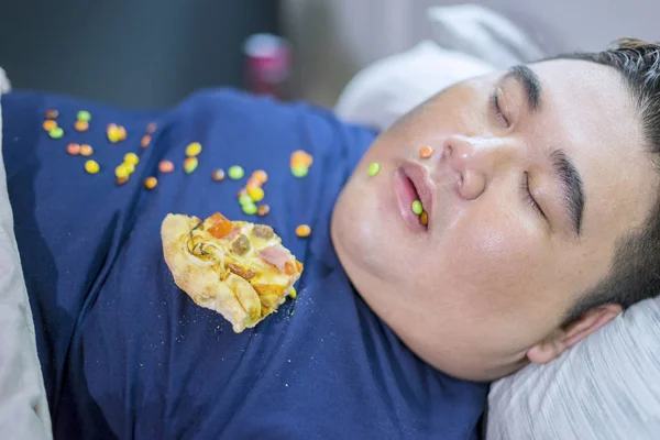 Fat man sleeping while junk foods scattered around — Stock Photo, Image