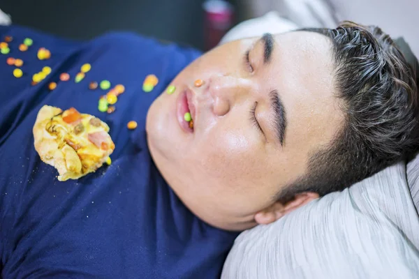 Fat man sleeping while pizza and candies scattered