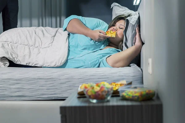Gruba kobieta je pizzę leżąc na łóżku — Zdjęcie stockowe