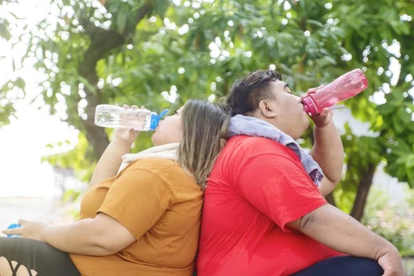 Portrait of fat couple chugging water at the park — Stock Photo, Image