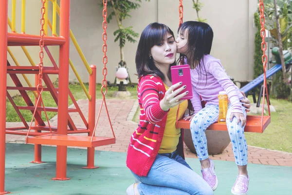 Schattig meisje zoenen haar moeder terwijl het nemen van een selfie — Stockfoto