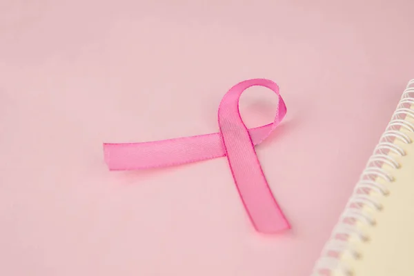 Pink ribbon lying beside a notebook in pink paper