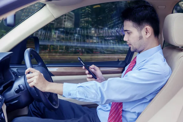 Podnikatel se dívá na svůj mobilní telefon v autě — Stock fotografie