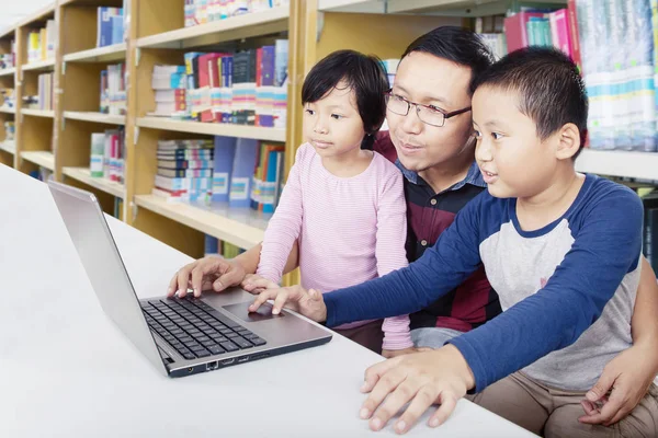 Pai ajuda seus filhos a aprender com um laptop — Fotografia de Stock