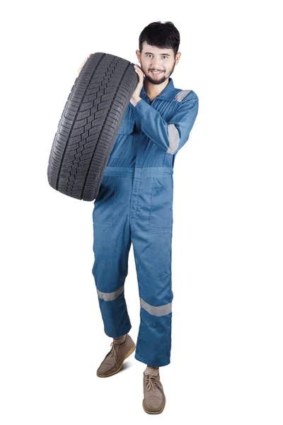 Joven mecánico llevando un neumático en el estudio — Foto de Stock