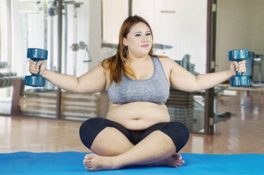 Kilolu kadın dambıllarla egzersiz yapıyor.