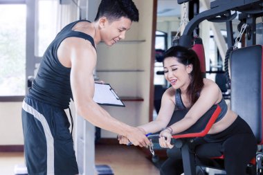 Antrenör, spor aletleri üzerinde egzersiz yapan kadına yardım ediyor.