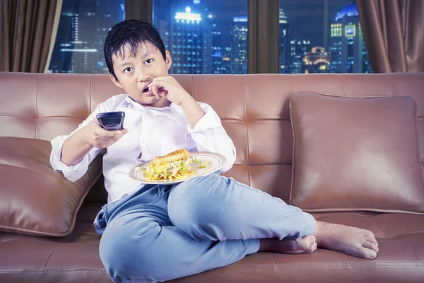 Niño viendo la televisión y disfrutando de la hamburguesa por la noche — Foto de Stock