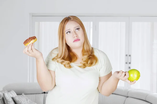 Kafası karışmış obez kadın ve donut ve elma meyvesi — Stok fotoğraf