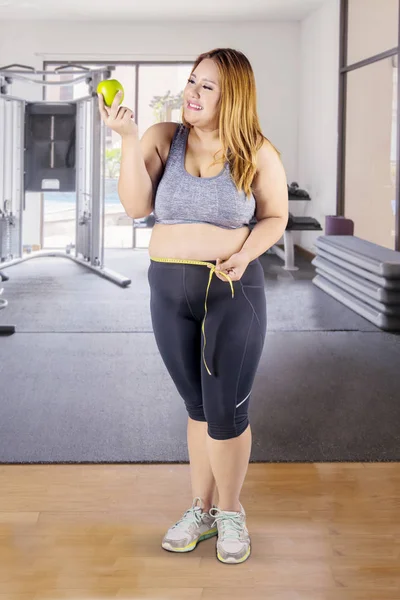 Ожирение женщина с яблоком и измерительной лентой в тренажерном зале — стоковое фото