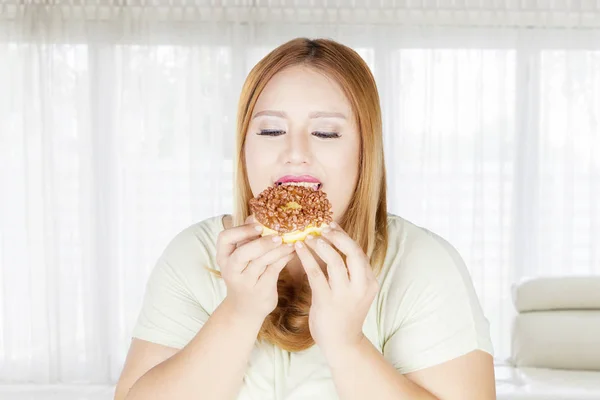Толстая женщина ест пончики дома — стоковое фото