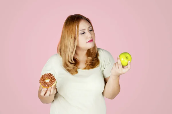 Kobieta z nadwagą z jabłkami i pączkami — Zdjęcie stockowe