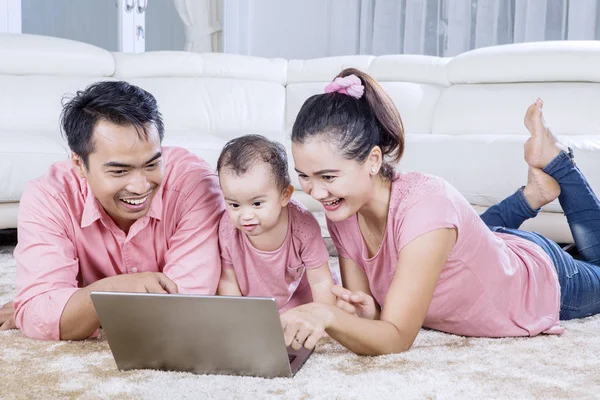 Родители и дочь используют ноутбук на ковре — стоковое фото