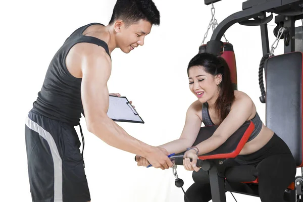 Woman exercising on gym equipment with trainer — Stock Photo, Image