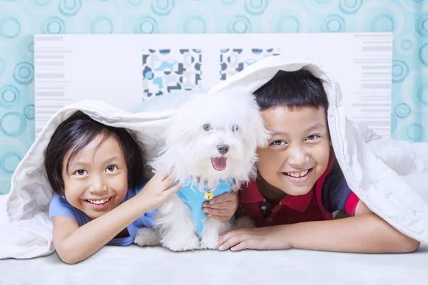 Dzieci uśmiechnięte do kamery z psem w sypialni — Zdjęcie stockowe