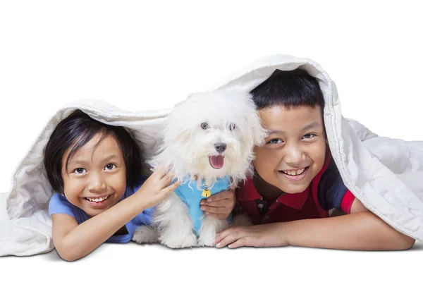 Bambini sorridenti a cam con il loro cane sotto coperta — Foto Stock