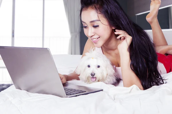 Mujer usando su portátil con su perro en el dormitorio — Foto de Stock