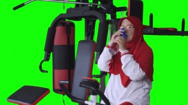 Olgun Müslüman kadın egzersiz bisikletinde su içiyor, video.