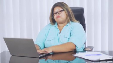 Genç şişman iş kadını ofiste dizüstü bilgisayarla çalışırken kalp krizi belirtileri gösteriyor. 4k çözünürlükte çekiliyor