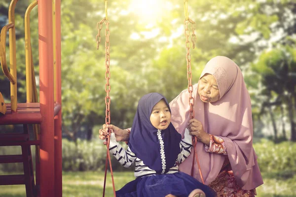 Mutlu Müslüman büyükanne ve torunu salıncakta oynuyorlar. — Stok fotoğraf