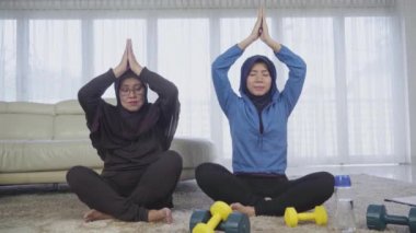 Yaşlı Müslüman kadın kızıyla yoga yapıyor.