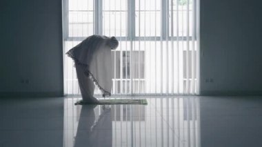 Pencerenin yanında namaz kılan yaşlı kadının yan görüntüsü
