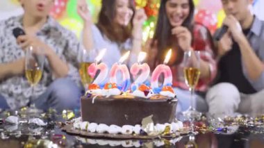 2020 yılbaşı mumlu doğum günü pastası bulanık mutlu insanların arka planında bir doğum günü partisini şenlikli dekorasyonla kutluyor. 4k çözünürlükte çekiliyor